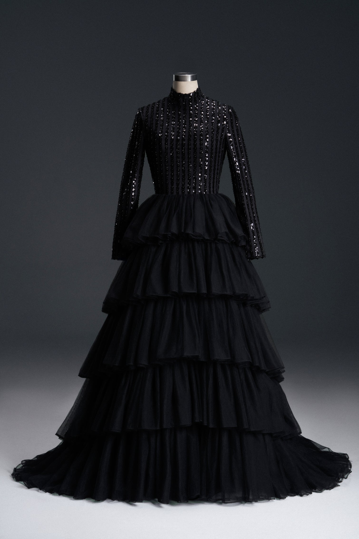 Elegant black evening gown featuring a sequined bodice with long sleeves and a high neckline. The voluminous ruffled tiered skirt adds dramatic flair, creating a sophisticated silhouette perfect for formal events, galas, and weddings.